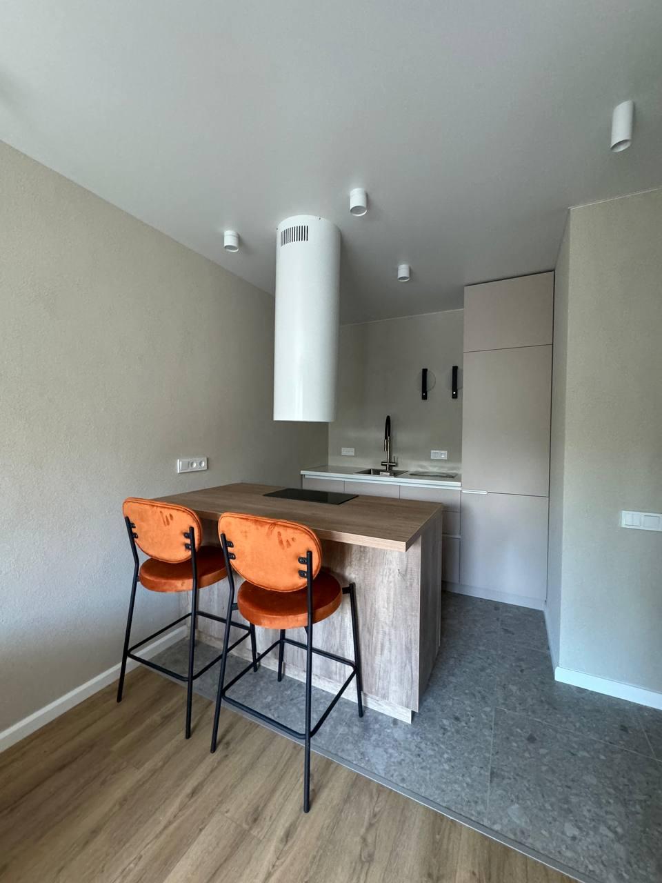 Кухня после ремонта: деревянный остров с оранжевыми стульями, граница керамогранита и ламината на полу